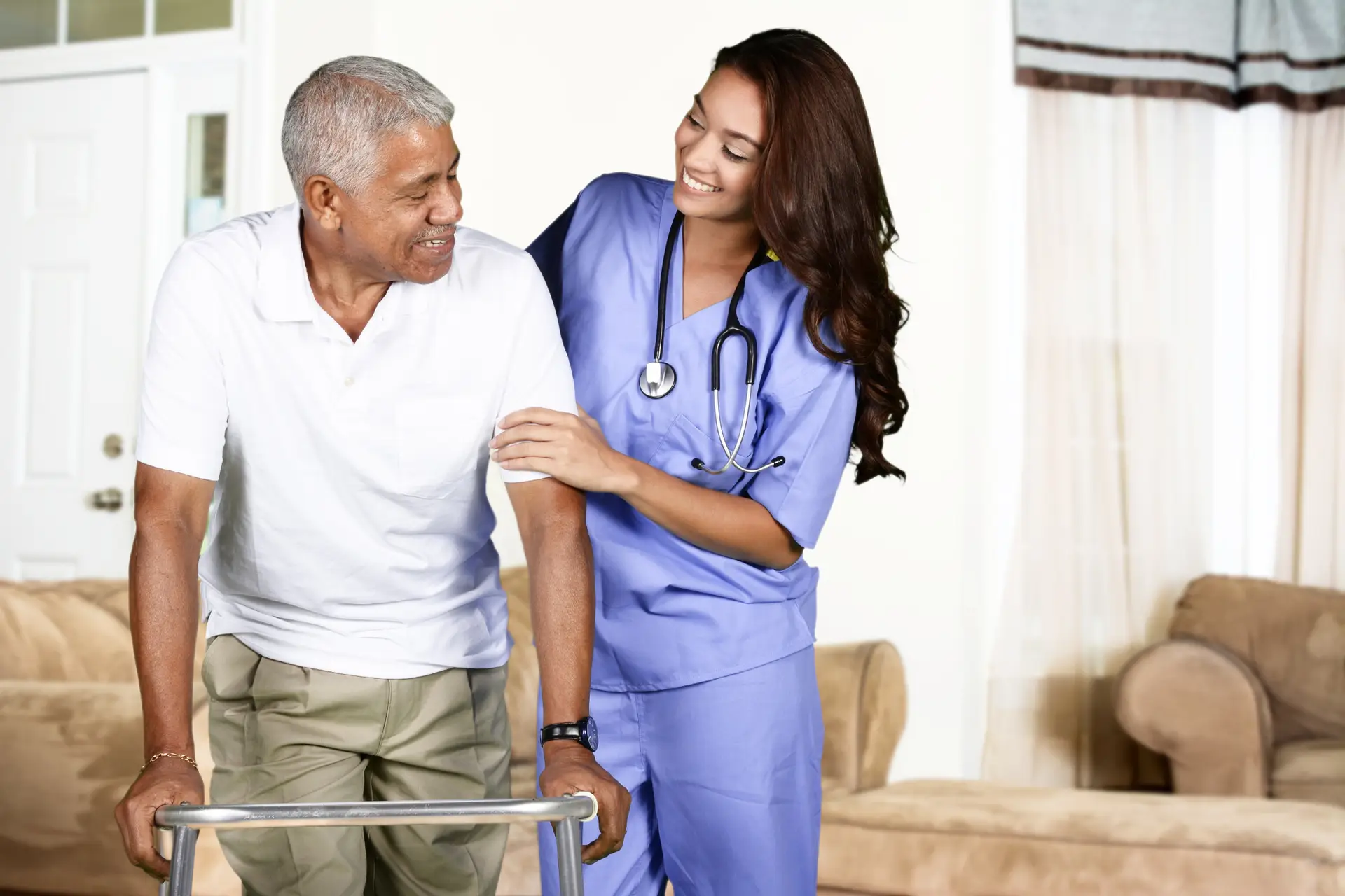 Health Care Worker and Elderly Man Premium Care Nurse in blue scrubs assists an elderly man using a walker in a living room smiling and offering support