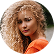 Woman with curly blonde hair in an orange top, looking toward the camera and smiling softly