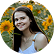 Smiling woman with long dark hair, wearing a white top, posing outdoors among sunflowers in a field.